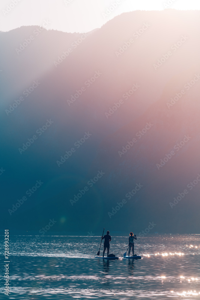 Couple paddle boarding at Lake Bohinj in summer, back lit image with lens flare