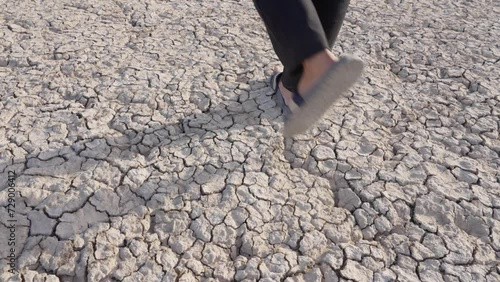 Handheld high angle shot of male feet with flip flops walking on extremely dry ground photo