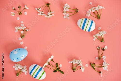 White flowers, cherry blossoms and Easter eggs with blue stripes on a pink background. Easter background, copy space. Flatlay