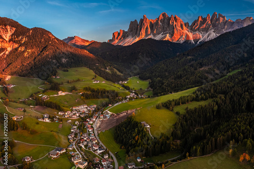 Val Di Funes, Dolomites, Italy - Aerial view of the Val di Funes province at South Tyrol with St. Johann church in San Valentino, the Italian Dolomites in warm sunset colors and blue sky at background photo