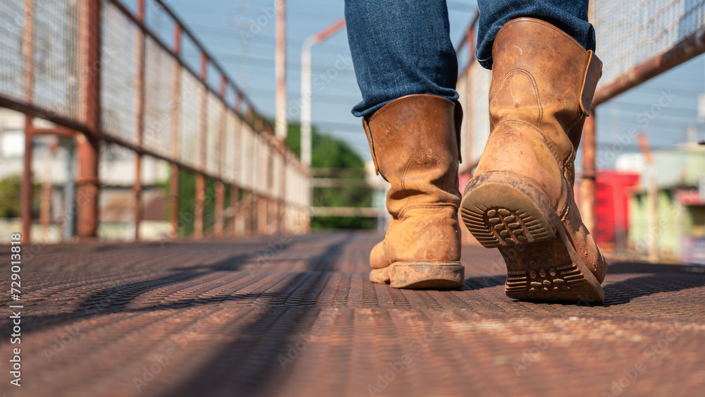 Close-up at worker feet is wearing leather safety boots during walking on rustic walkway platform. Ready to working in the challenge industrial concept scene. Close-up at worker feet is wearing leather safety boots during walking on rustic walkway platform. Ready to working in the challenge industrial concept scene.