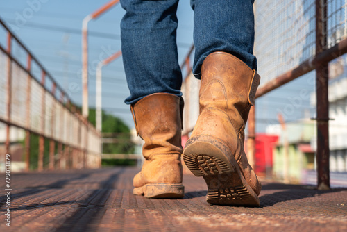 Close-up at worker feet is wearing leather safety boots during walking on rustic walkway platform. Ready to working in the challenge industrial concept scene.