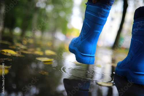 legs of child in blue rubber boots jumping in the autumn puddles photo