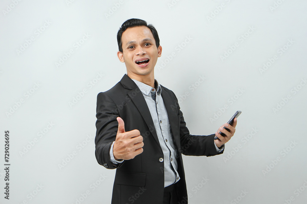 portrait of asian indonesian business man in suit holding smart phone with smlie and thumb up finger gesture on isolated background portrait of asian indonesian business man in suit holding smart phone with smlie and thumb up finger gesture on isolated background