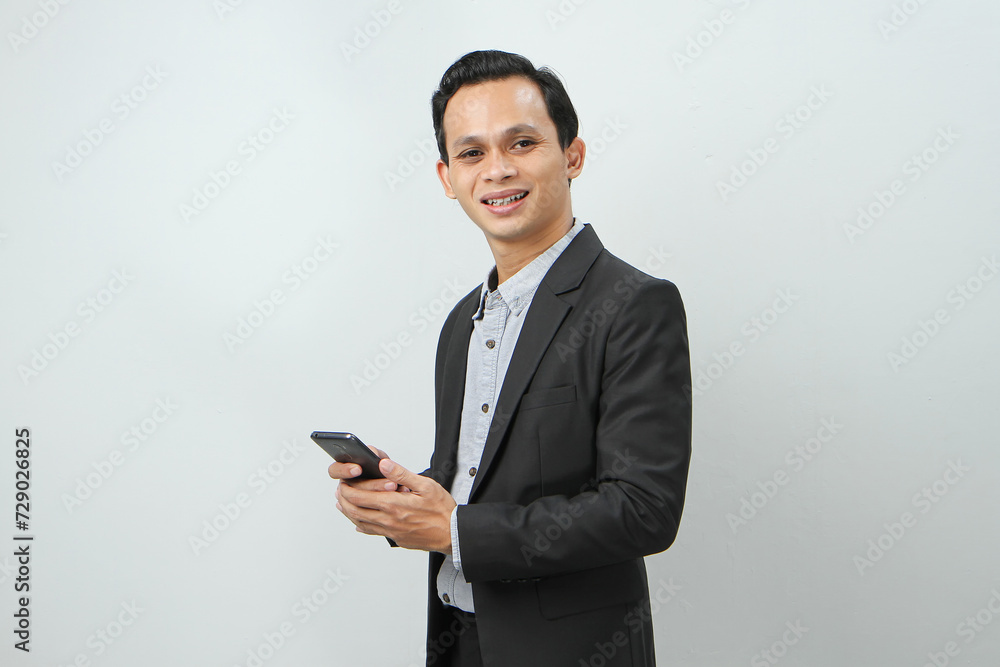 happy asian indonesian business man in suit holding smart phone on isolated background happy asian indonesian business man in suit holding smart phone on isolated background