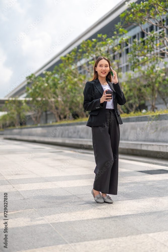 Young Asian Woman holding coffee cup and using phone outdoor in a central business district area Young Asian Woman holding coffee cup and using phone outdoor in a central business district area