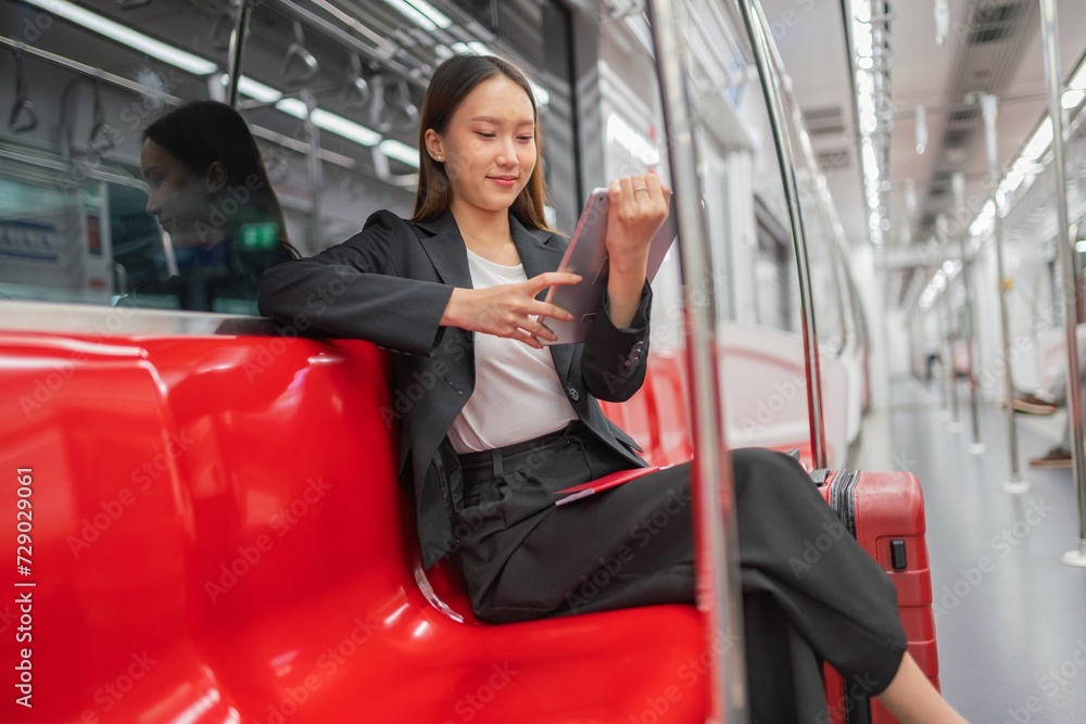 Young asian businesswoman traveling to airport on skytrain checking information using her digital tablet Young asian businesswoman traveling to airport on skytrain checking information using her digital tablet
