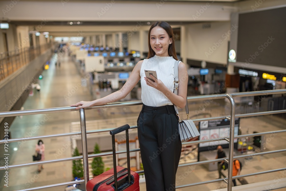 Young asian businesswoman using phone and holding passport getting ready to travel at the airport departure hall terminal Young asian businesswoman using phone and holding passport getting ready to travel at the airport departure hall terminal