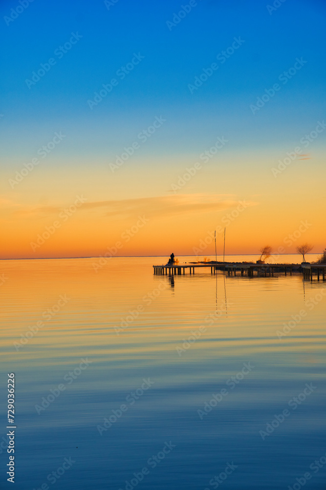 Person standing on a pier over a lake at sunrise