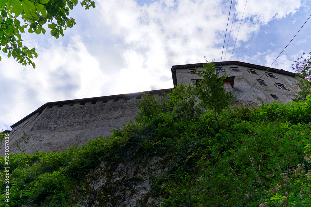 Looking up stone wall and tower of castle on a rock with cables of cable car at Slovenian City of Bled on a blue cloudy summer day. Photo taken August 8th, 2023, Bled, Slovenia.