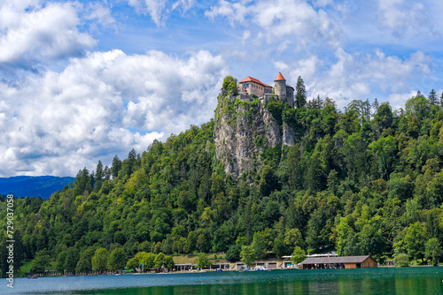 Castle on top of rock with waving Slovenian flag at lakeshore of Slovenian Lake Bled on a blue cloudy summer day. Photo taken August 8th, 2023, Bled, Slovenia.