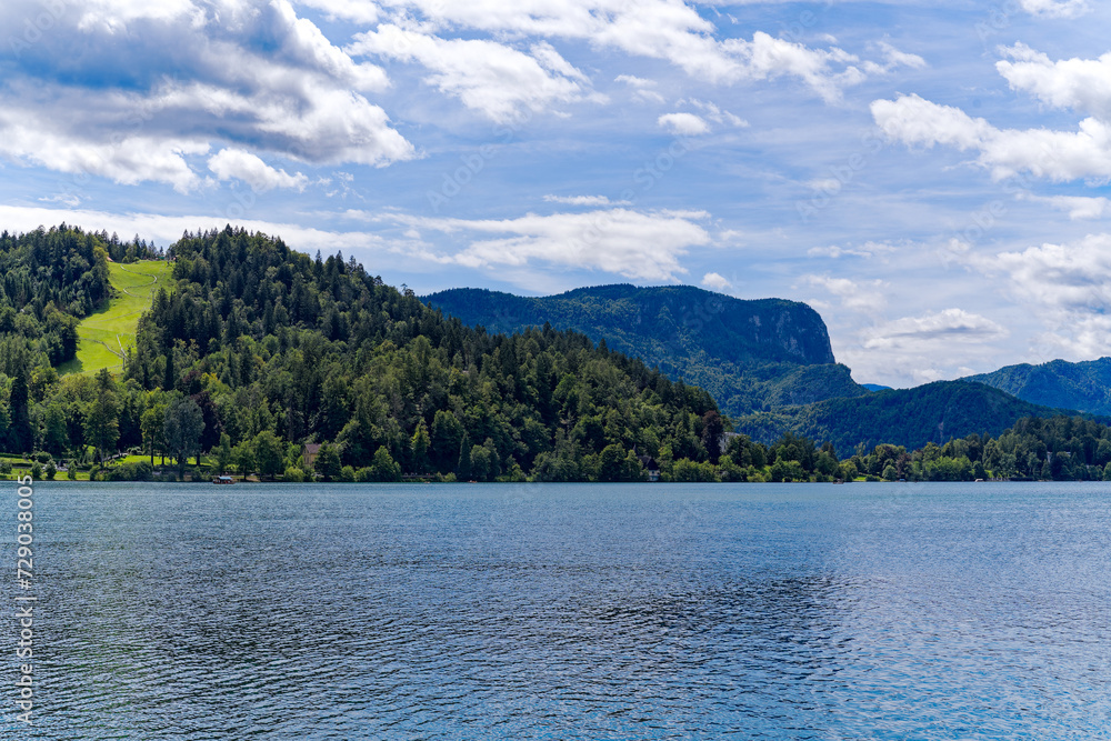 Lake Bled with woodland and mountain panorama in the background on a cloudy summer day. Photo taken August 8th, 2023, Bled, Slovenia.