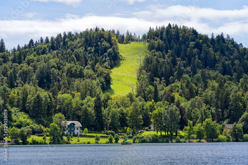 Scenic view of Lake Bled with beautiful reflections and mountain with chair lift and tobogganing in the background on a blue cloudy summer day. Photo taken August 8th, 2023, Bled, Slovenia. photo