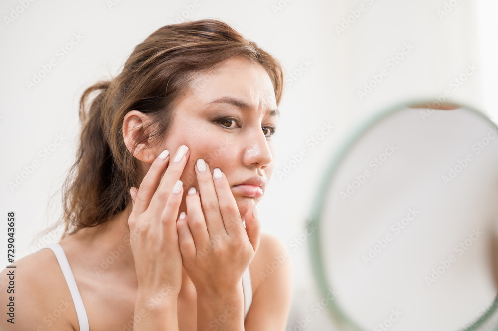 Young beautiful Asian woman checking her facial skin in mirror feeling worried about freckles wrinkles acne scar on face. Lady beauty self care skincare problem solution product advertising concept. Young beautiful Asian woman checking her facial skin in mirror feeling worried about freckles wrinkles acne scar on face. Lady beauty self care skincare problem solution product advertising concept.