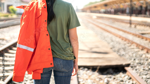 Close-up at a lady back during take a working uniform over the shoulder with background of the railway (train logistic workplace). Ready to working in challenge industrial concept scene.