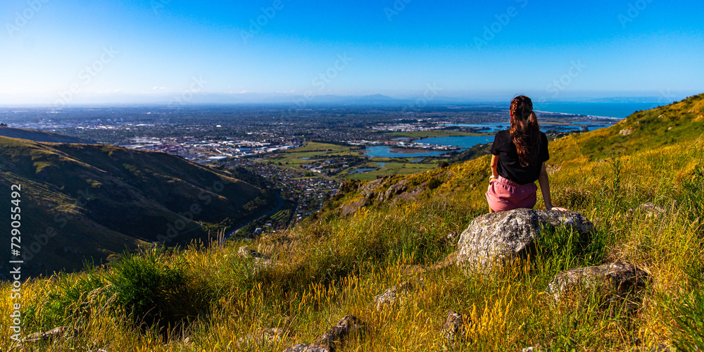 pretty girl sitting at the top of hill and watching the panorama of christchurch; hiking bridle path in christchurch