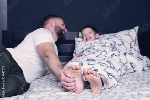 Bare feet of a child. Dad tickles his child's feet sticking out from under the blanket. Laughter and joy of father and son. photo