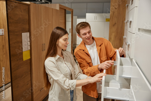 Young family shopping at furniture store selecting cabinet with drawers for kitchen