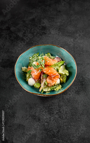 Salad with salmon, mozzarella, and avocado, served in a turquoise ceramic bowl