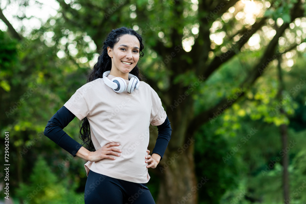 Proud mixed woman with long curly hair and sporty uniform standing outdoors with hands on waist. Satisfied young lady completed daily workout and feeling motivated for achieving bigger results. Proud mixed woman with long curly hair and sporty uniform standing outdoors with hands on waist. Satisfied young lady completed daily workout and feeling motivated for achieving bigger results.