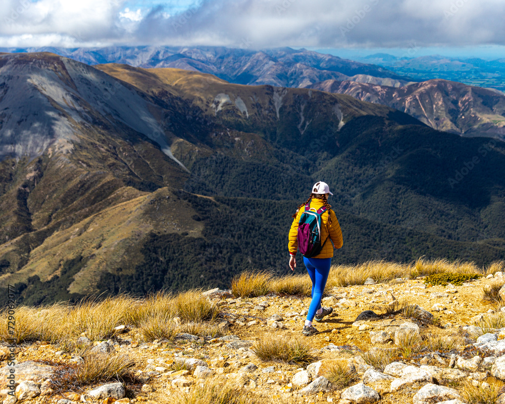 Obraz premium hiker girl walking down the steep trail from the top of mount somers in canterbury, new zealand south island