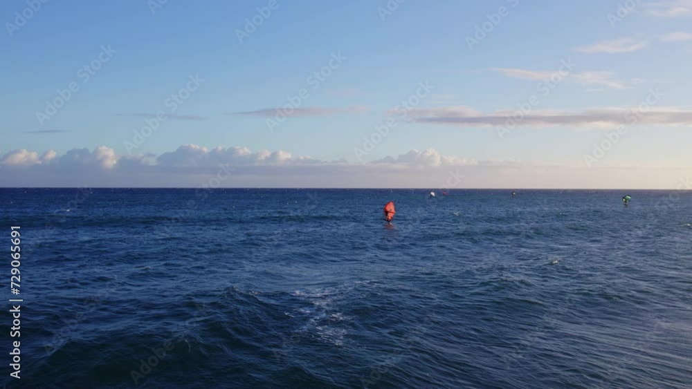 a kiteboarder glides across the blue water of the Pacific ocean as the white capped waves crash to the shore in Hawaii