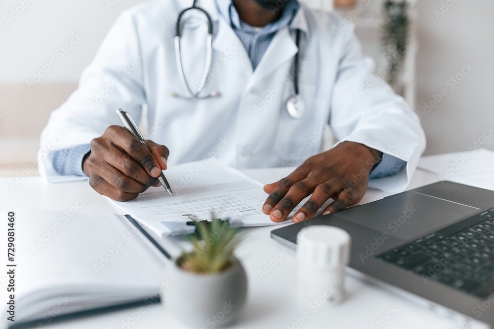 Writing information into the document. Black man as doctor in the clinic office Writing information into the document. Black man as doctor in the clinic office