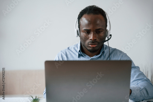 In headphones. Businessman is working in the office by laptop