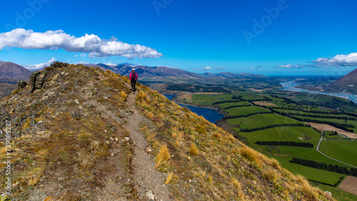 backpacker walking alongside a ridge and admiring the panorama of southern alps from the summit of peak hill, canterbury, new zealand south island photo