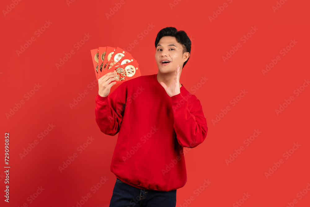 Excited handsome Asian man holding red envelopes isolated red background Excited handsome Asian man holding red envelopes isolated red background
