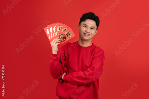 Smiling handsome Asian man holding red Ang Pao in studio isolated red background for Chinese new year concepts photo