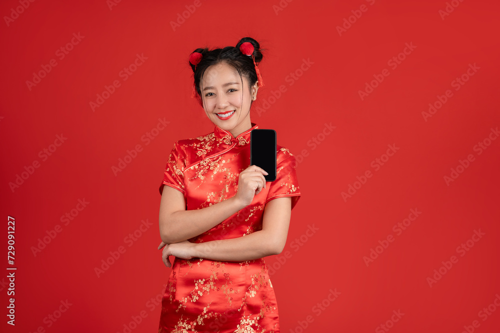 Happy Asian woman wearing qipao dress and showing smartphone isolated on red background. Happy Asian woman wearing qipao dress and showing smartphone isolated on red background.
