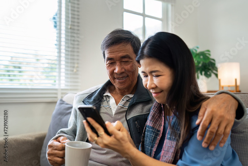 Retired elderly couple sits on couch drink tea and using mobile together and relax in their home. Senior Activity Concept