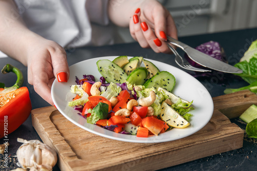 A plate with chopped fresh vegetables in female hands in the kitchen.