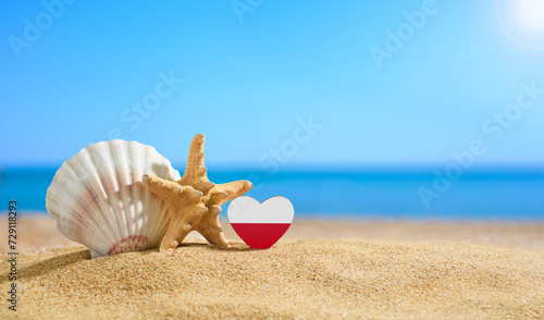 Poland flag in the shape of a heart and shells on a sandy beach. photo