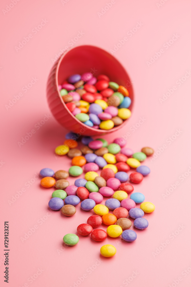 Colorful sweet candies in bowl on pink background.