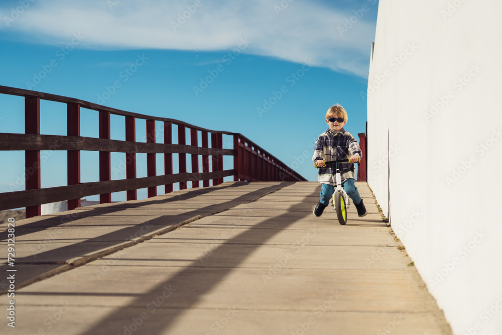 Cute little boy rides a jogging bike down the road on a sunny day, the child plays and rides his bike.