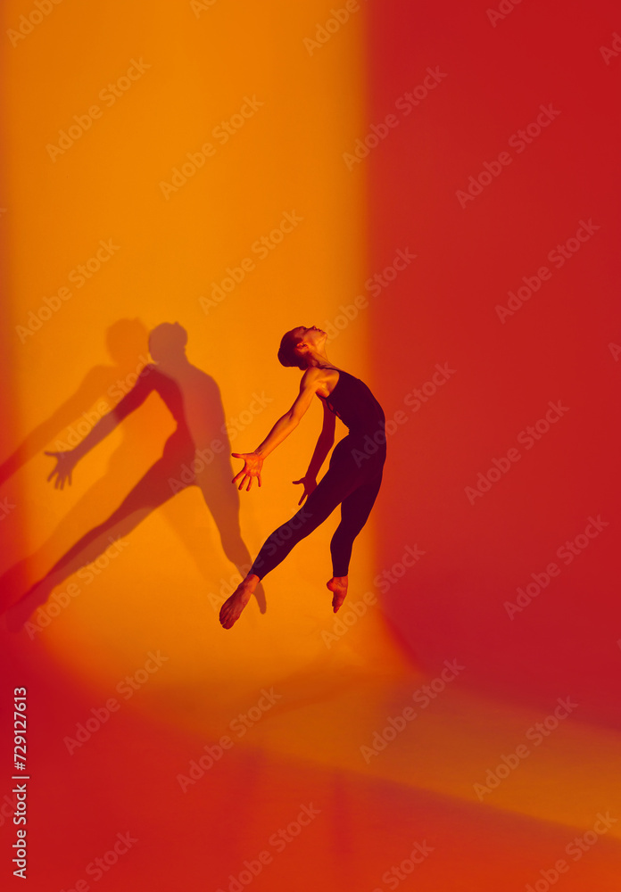 Athletic Beauty in Motion. Portrait of beautiful ballerina dances in black sports overalls, barefoot in neon-lit studio, her movements fluid against gradient background. Concept of athleticism, beauty