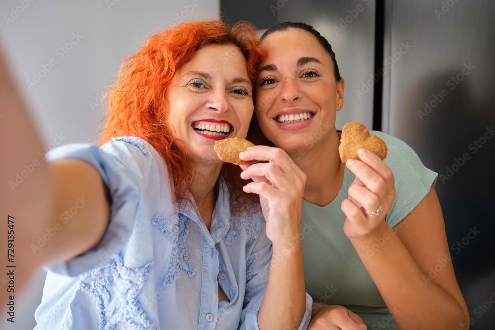 Mother and daughter taking a selfie while eating homemade butter cookies. Family time.