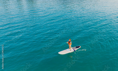 Happy Asian young woman standing on a sup Surfing balancing on supboard paddling with water sea background