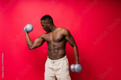 Young man with dumbbells good physique isolated on red and black background. Strength and motivation photo