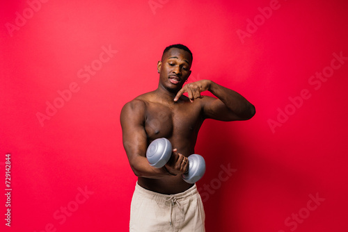 Young man with dumbbells good physique isolated on red and black background. Strength and motivation