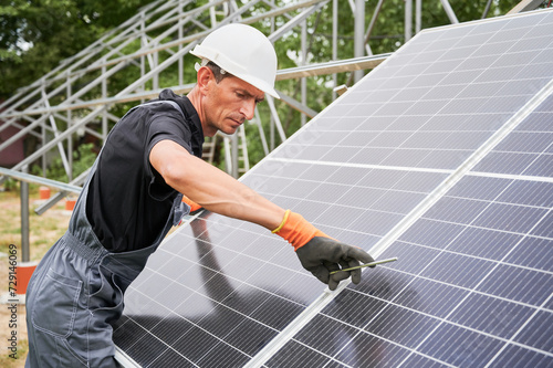 Man technician installing photovoltaic solar panels. Male worker in safety helmet fixing solar module on supporting structure while mounting photovoltaic panel system.