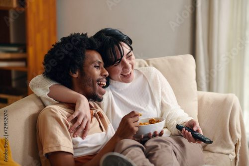Photography Young laughing man with bowl of popcorn and his wife with remote control sitting