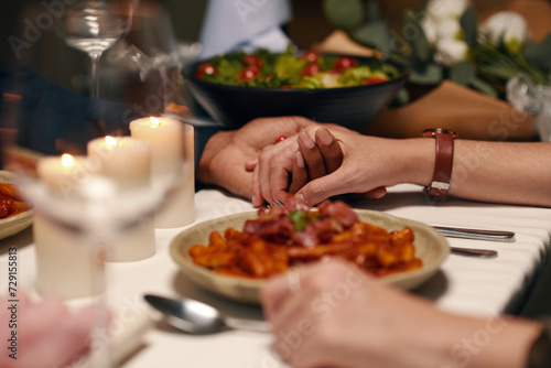 Hands of young intercultural affectionate valentines sitting by served table in front of camera and enjoying festive dinner at home or restaurant