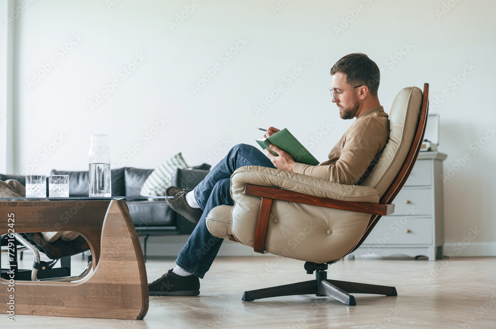 Male psychologist is sitting in the chair with notepad in the office