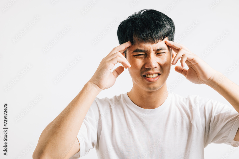 An Asian man, overwhelmed by stress and suffering from a painful headache, holds his head with a sad expression. Studio shot isolated on white, highlighting his discomfort and illness. An Asian man, overwhelmed by stress and suffering from a painful headache, holds his head with a sad expression. Studio shot isolated on white, highlighting his discomfort and illness.