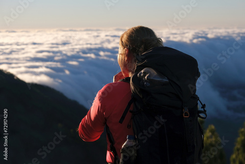 Woman with backpack is looking to mountain panorama with clouds in sunrise. Refugio Punta de Los Roques, Caldera de Taburiente. La Palma, Canary Islands, Spain 