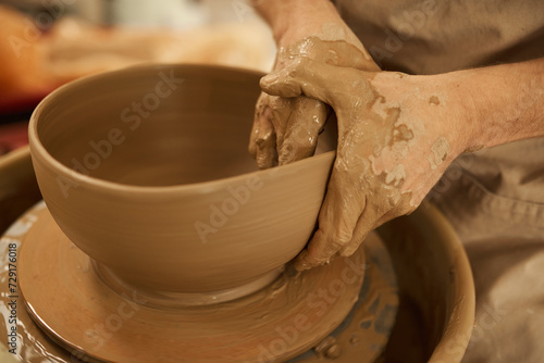 Ceramist making a bowl with his hands on a wheel in a studio © mavoimages