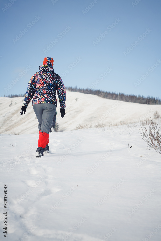 Woman in winter clothes walking through a snowy field toward a hill